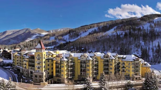 Un hotel a più piani con facciata gialla, situato in una zona montuosa con paesaggi innevati.