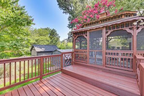 A wooden deck with a covered area, surrounded by greenery and a small shed.