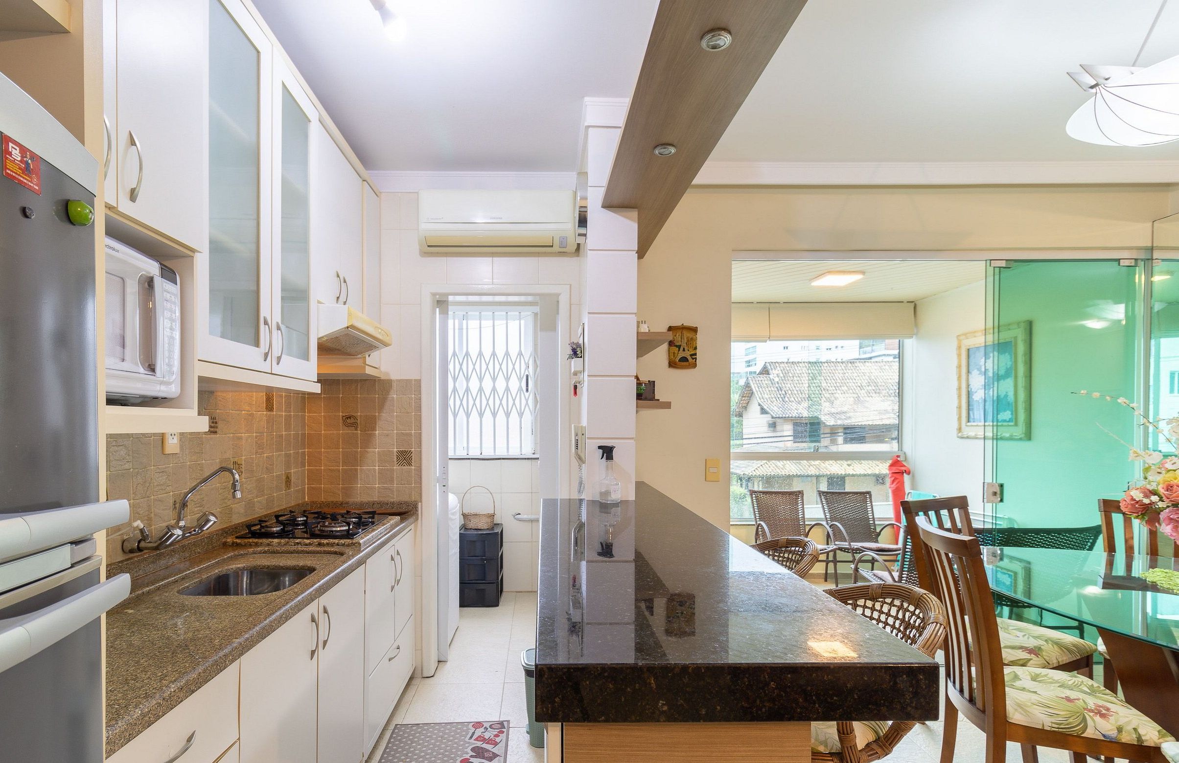 A modern kitchen with a granite countertop, stainless steel appliances, and a dining area with a glass table and wooden chairs.