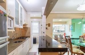 Una cocina moderna con encimera de granito, electrodomésticos de acero inoxidable y un comedor con mesa de vidrio y sillas de madera.