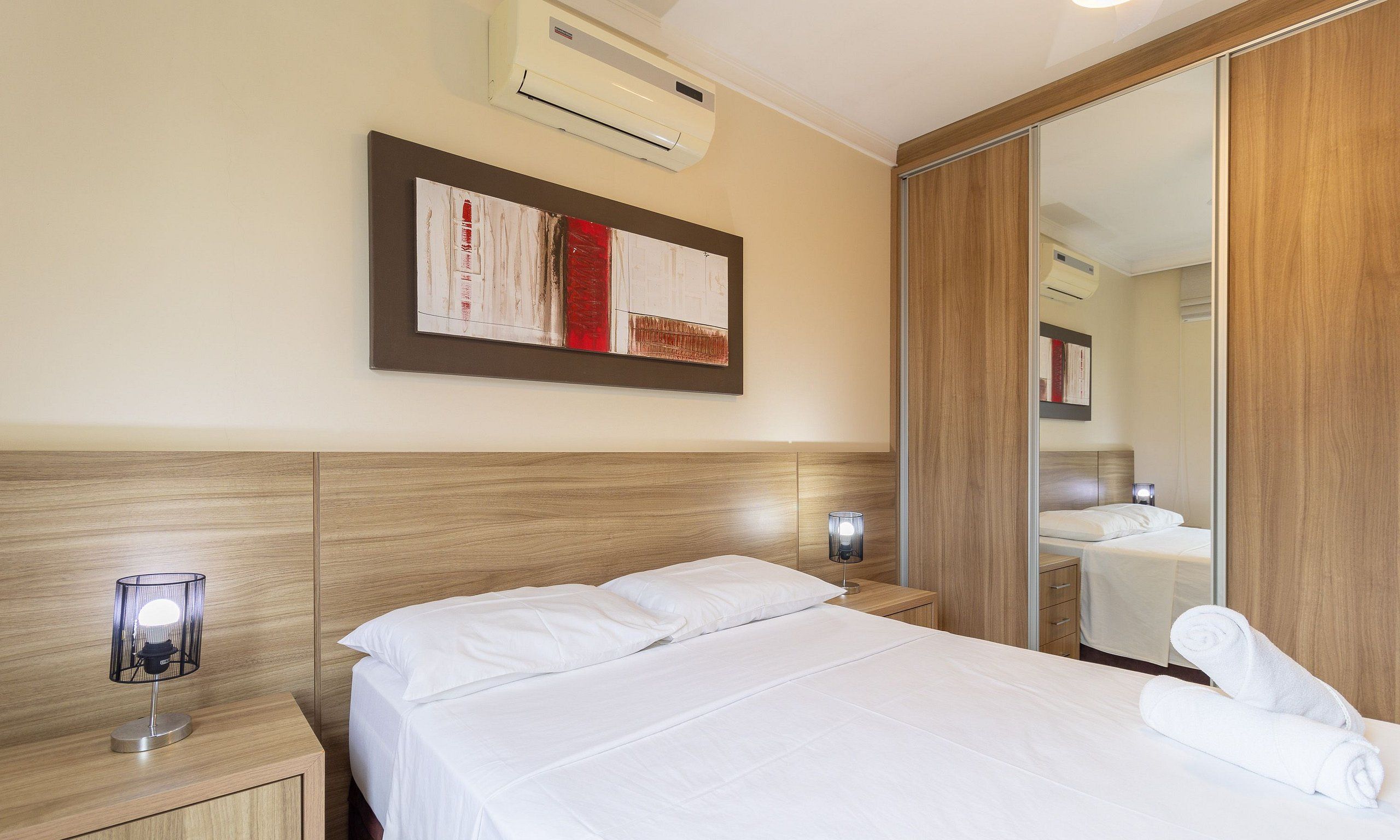 Et hotelværelse med en seng, et natbord, en lampe, et spejl og en aircondition.