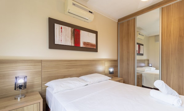 Habitación de hotel con cama, mesita de noche, lámpara, espejo y unidad de aire acondicionado.