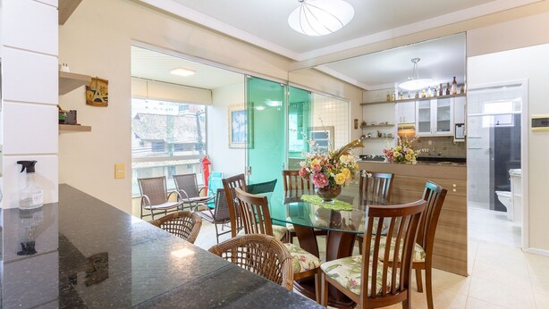 Una cocina moderna con armarios blancos, una isla de vidrio y un comedor con sillas de mimbre y una mesa de vidrio.