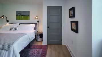 A bedroom with a bed, bedside lamps, a rug, a door, and wall art.