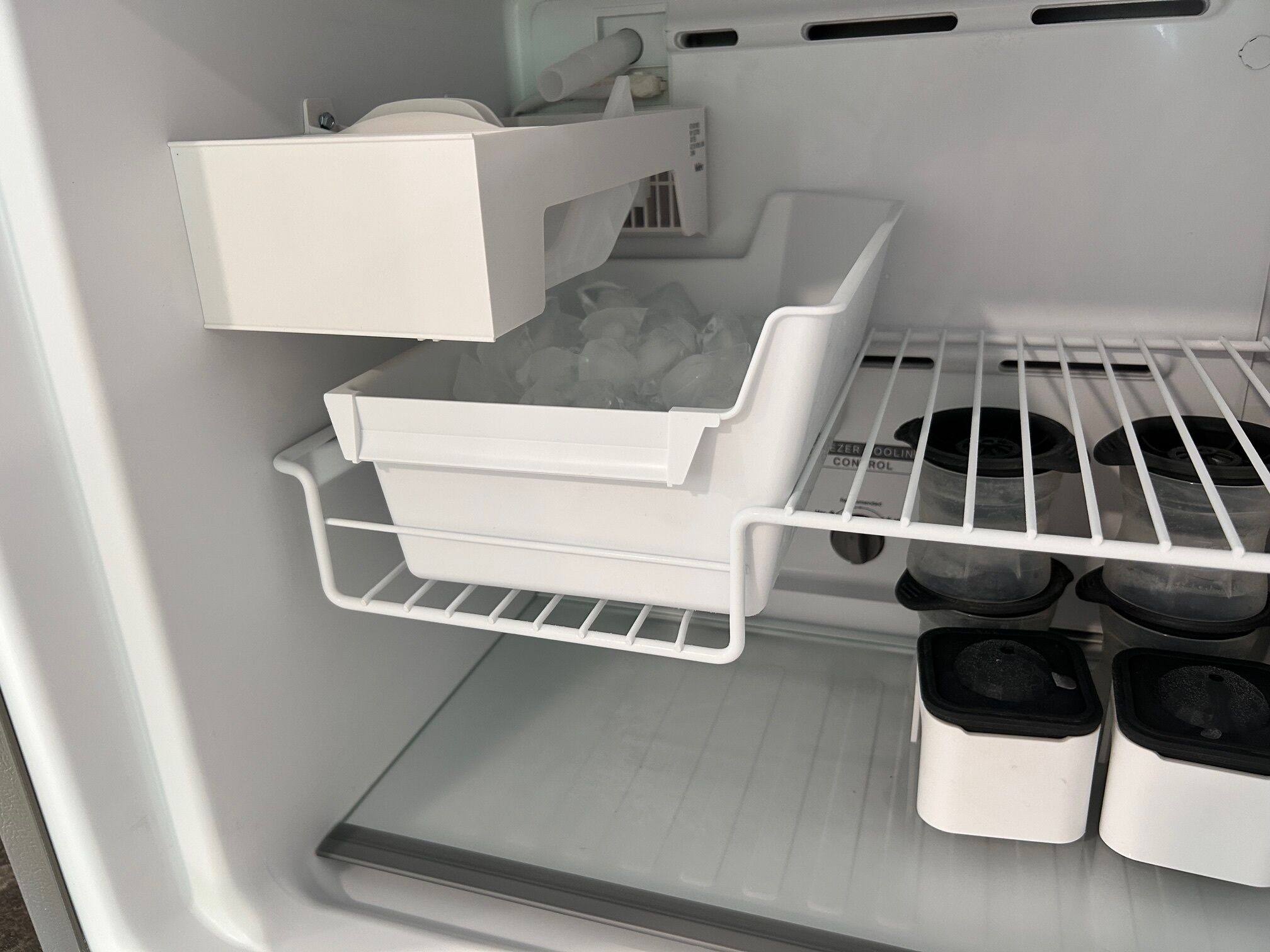 A refrigerator with a freezer compartment, a built-in ice maker, and shelves for storing food containers.