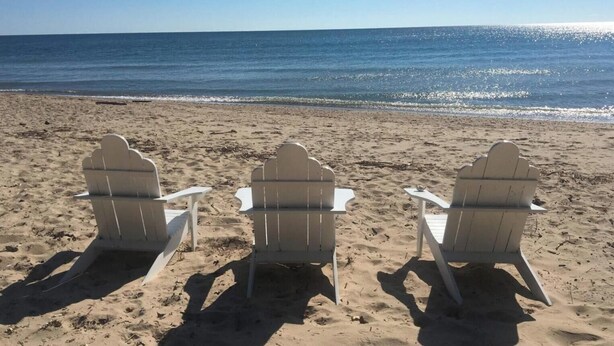 Tres sillas Adirondack sobre una playa arenosa con vista al océano.