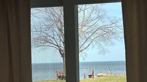 Vista a través de una ventana que muestra un área con césped, un banco y una masa de agua.