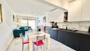 A modern kitchen with a marble countertop, a dining area with a table and chairs, and a living area with a sofa and a TV. - 100M FROM THE CASINO, LOVELY 3-ROOM APARTMENT WITH SEA VIEW AND BIJOU GARDENS. PRIVATE PARKING. (Menton)