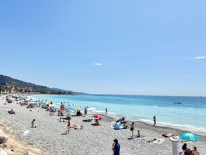 A crowded beach with people sunbathing and swimming, umbrellas, and a tent.