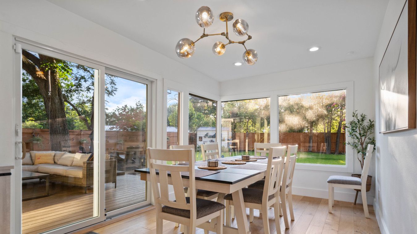 A spacious dining area with a wooden table and chairs, large windows offering views of the backyard, and a modern chandelier.