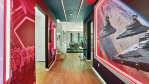 Un pasillo con diseño moderno, suelo de madera y paredes rojas con patrones geométricos iluminados. Se observa un comedor al fondo con una mesa y sillas.