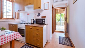 A compact kitchen with wooden cabinets, a gas stove, a microwave, and a small dining table with a checkered tablecloth.