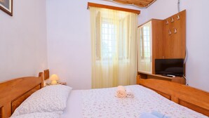 A bedroom with two wooden beds, a TV on a wooden cabinet, and a window with curtains.