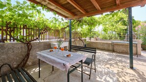 An outdoor patio with a table set for two, surrounded by greenery and a wooden pergola.