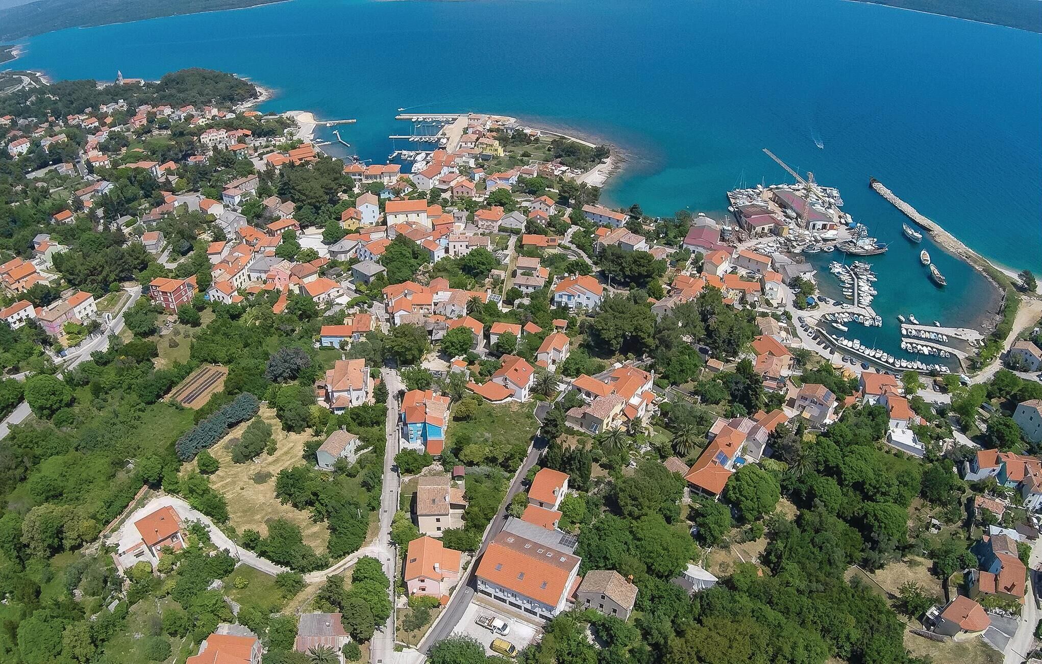 Vista aérea de un pueblo costero con edificios residenciales, un puerto deportivo y un mar azul cristalino.