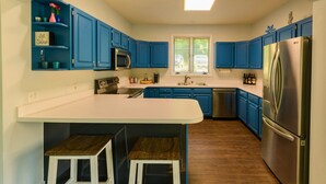 Una cocina moderna con armarios azules, un refrigerador de acero inoxidable y una isla central con taburetes.