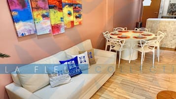 Uma sala de estar moderna com sofá, mesa de jantar e cadeiras, e arte abstrata colorida na parede.