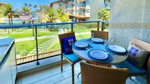 A balcony with a table set for four, overlooking a pool and resort buildings. - La Fleur Collection Vacation Homes (Ipojuca)