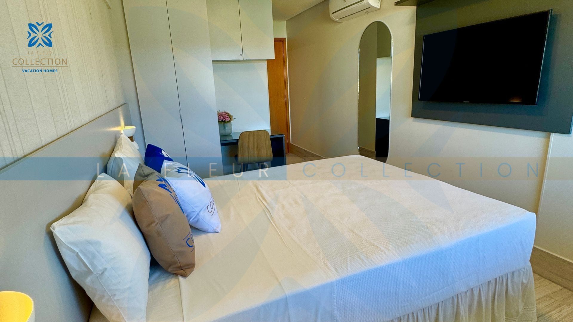 A hotel room with a bed, a desk, a chair, and a TV mounted on the wall.