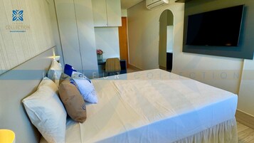 A hotel room with a bed, a desk, a chair, and a TV mounted on the wall.