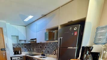 A compact kitchen with a refrigerator, sink, and a water dispenser.