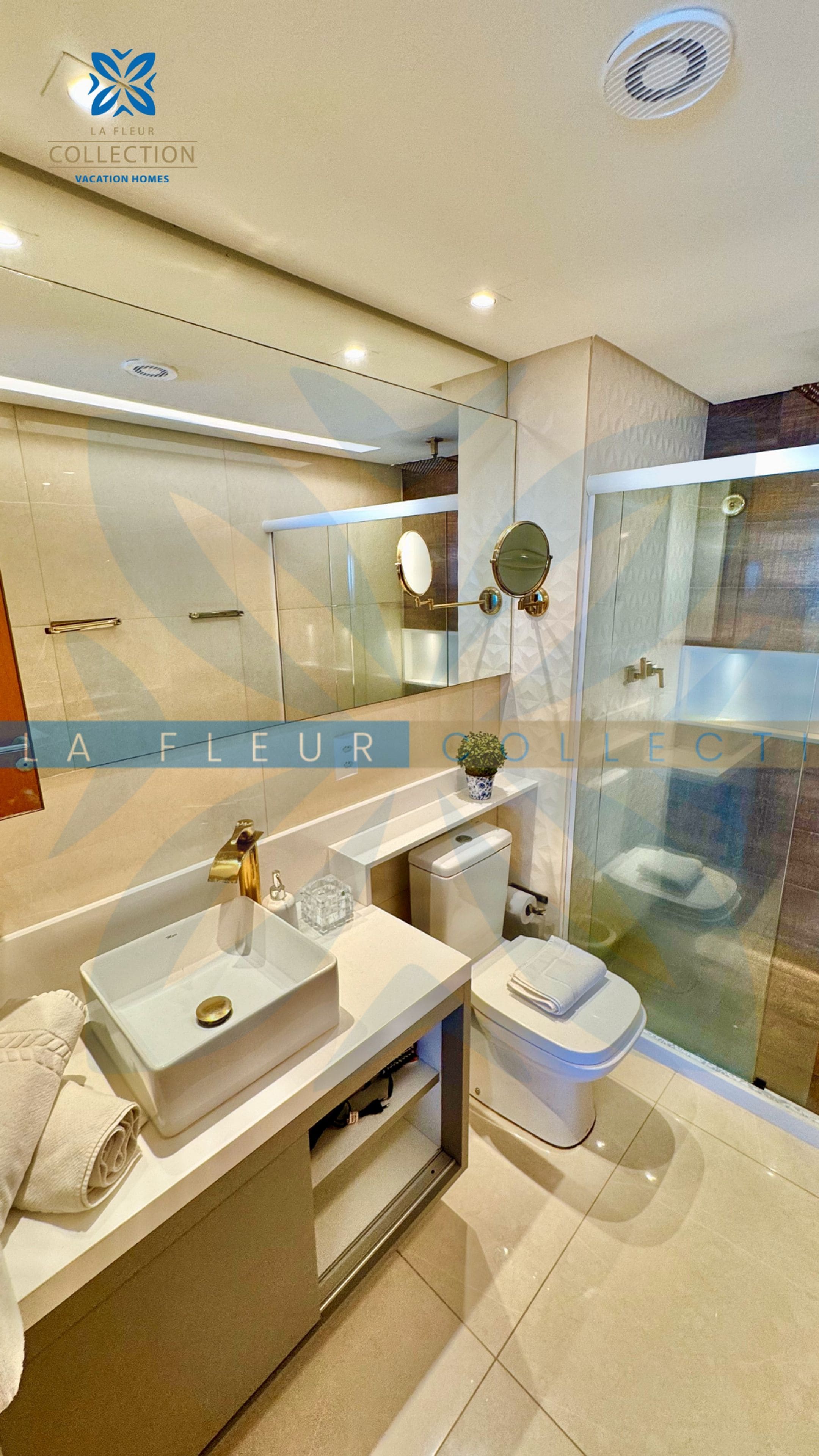 Un baño moderno con cabina de ducha de vidrio, tocador con lavamanos y espejo, y un inodoro.