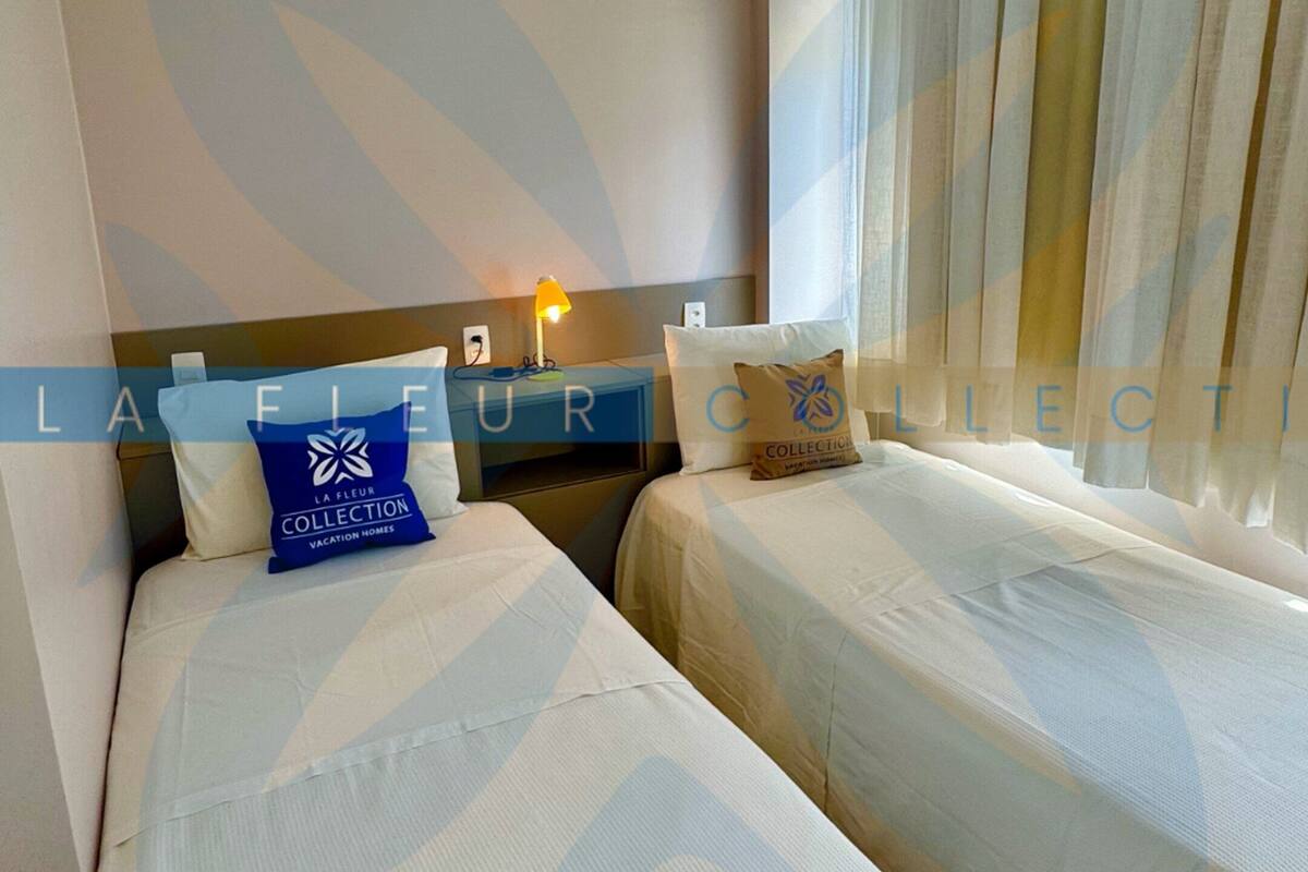Ein Hotelzimmer mit zwei Betten, einem Nachttisch, einer Lampe und einem Fenster mit Vorhängen.