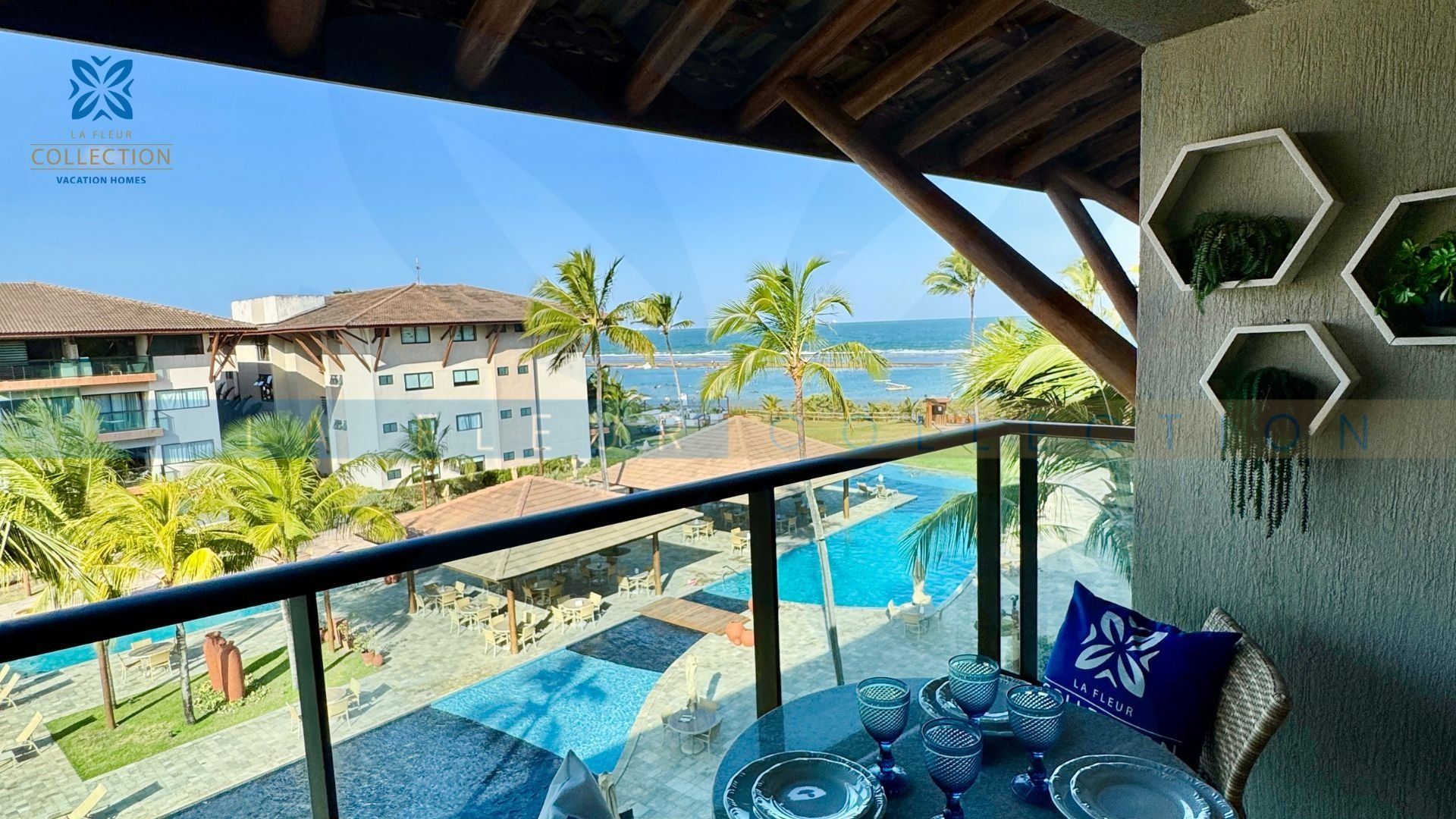 A balcony with a pool, palm trees, and a view of the ocean.