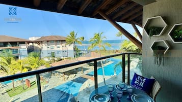 A balcony with a pool, palm trees, and a view of the ocean.
