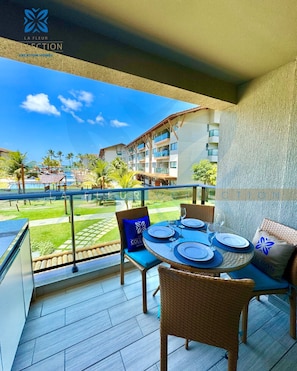 A balcony with a table set for four, overlooking a pool and resort buildings. - La Fleur Collection Vacation Homes (Ipojuca)