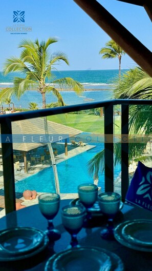 A poolside view with a clear view of the ocean, palm trees, and a lounge area with tables and chairs. - La Fleur Collection Vacation Homes (Ipojuca)