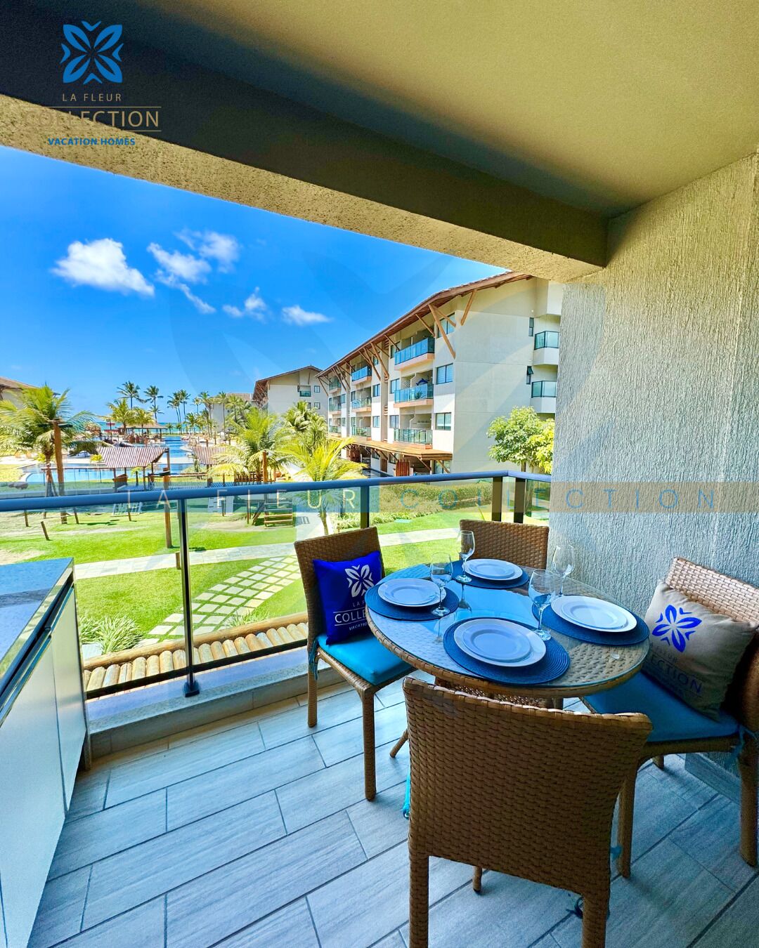 Un balcón con una mesa preparada para cuatro personas, con vistas a una piscina y edificios del resort.