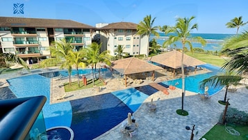 Um hotel com área de piscina, palmeiras e vista para o oceano.