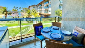 A balcony with a table set for four, overlooking a pool and resort buildings. - La Fleur Collection Vacation Homes (Ipojuca)