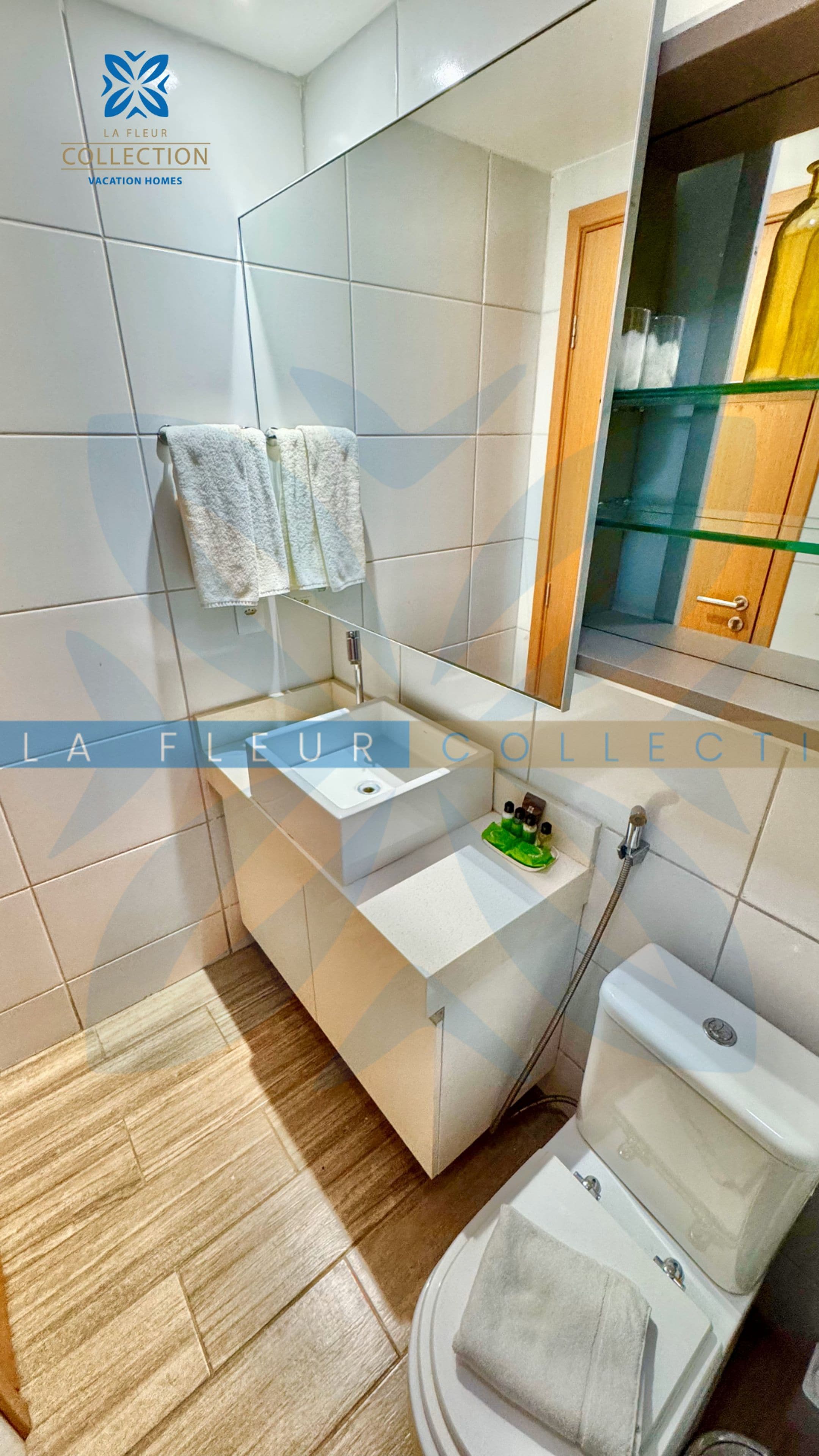 Een moderne badkamer met een wit wastafel, spiegel en toilet. Twee handdoeken hangen aan de muur.