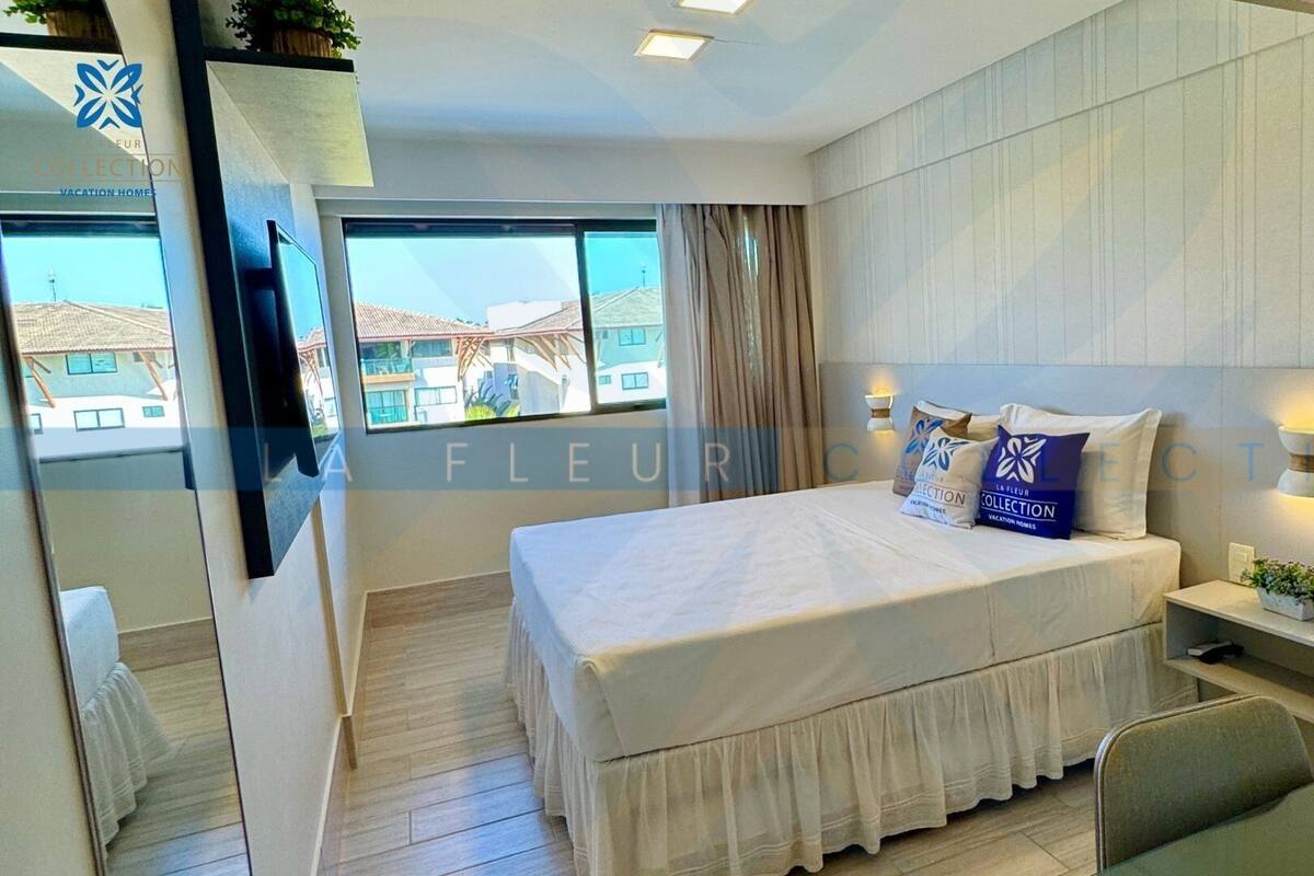 A modern bedroom with a large bed, a bedside table, a chair, and a window with a view of buildings.