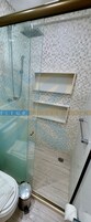 Un baño con ducha de vidrio, paredes de azulejos, inodoro y un cubo de basura.