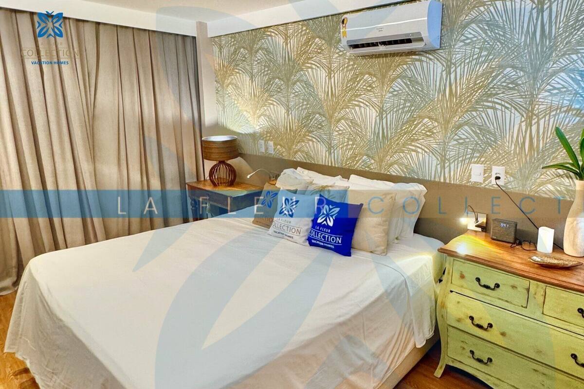 A bedroom with a bed, a nightstand, a lamp, and a wall air conditioner.