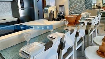 A modern kitchen with a central island, pendant lighting, and a dining area with chairs and tables.
