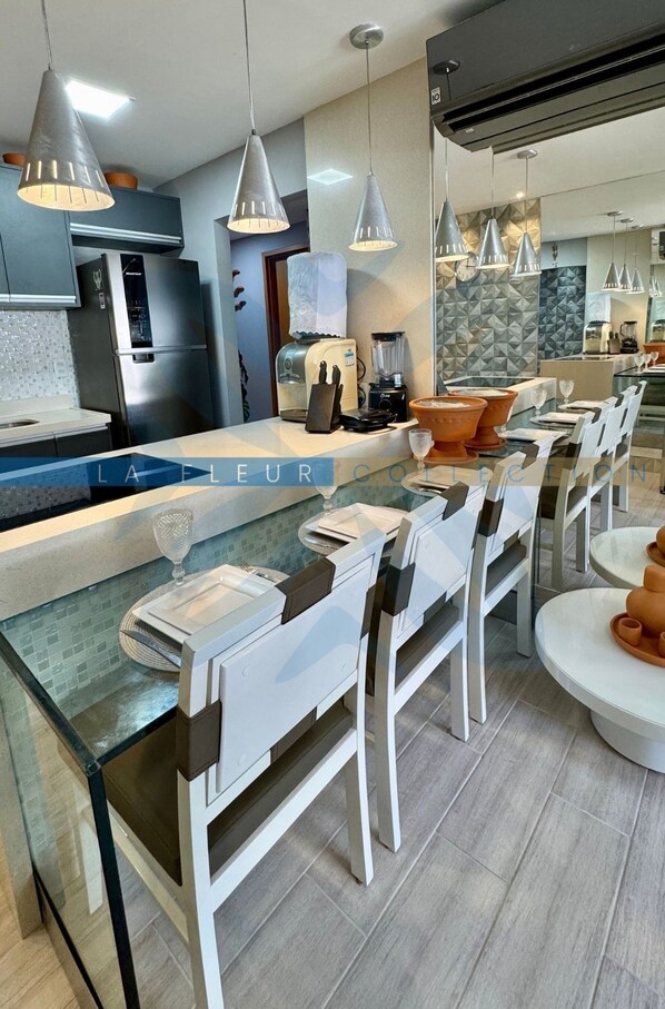 A modern kitchen with a central island, pendant lighting, and a dining area with chairs and tables. - La Fleur Collection Vacation Homes (Ipojuca)