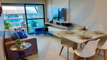 A modern living room with a sofa, a dining table set for four, and a TV mounted on the wall.