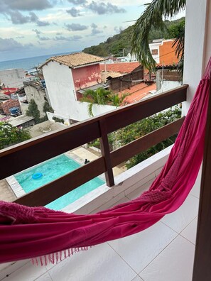 Un balcón con una hamaca, una piscina y vistas de la ciudad.