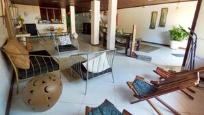 A spacious living area with a high ceiling, wooden flooring, and a mix of seating options including a round table, a metal chair, and wooden chairs. - Pousada Praiana Pipa (Tibau do Sul)