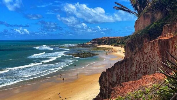 A beach with clear blue water, a sandy shore, and a rocky cliff. - Pousada Praiana Pipa (Tibau do Sul)