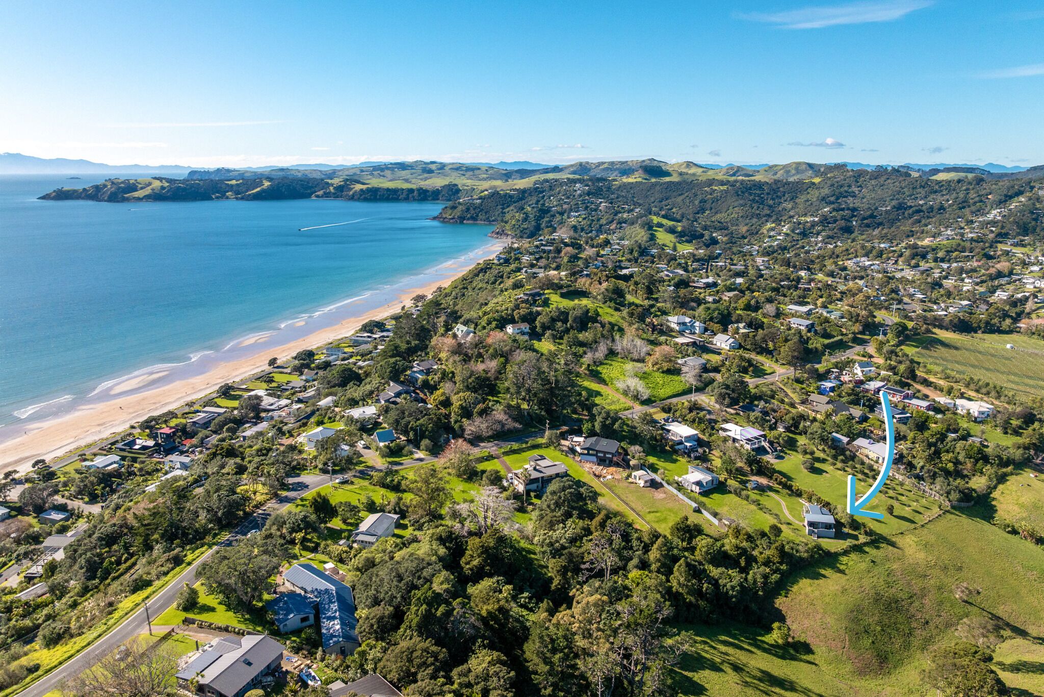 An aerial view of a coastal residential area with houses, green spaces, and a beach.