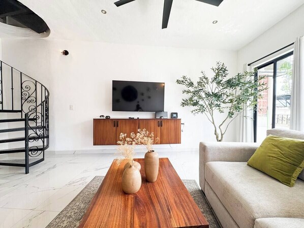 A modern living room with a wooden coffee table, a sofa, a TV mounted on a wooden cabinet, and a staircase with a decorative railing. - A Comfortable Stay: The Ocean, the Hotel District, and the Stadium (Puerto Vallarta)