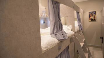 A hotel room with bunk beds, a bedside table with a lamp, and a painting on the wall.