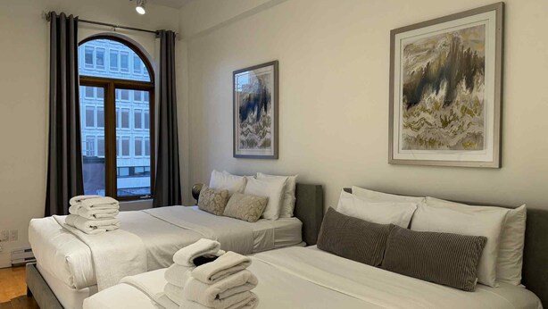A hotel room with two beds, a large window with curtains, and two framed artworks on the wall. - La Galerie Privée Luxe & Impeccable Stay (Montréal)