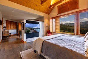 A bedroom with a large bed, a TV, wooden ceiling beams, and a view of mountains. - Telluride Modern Estate | Panoramic Mountain Views (Telluride)