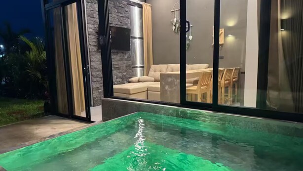 A modern outdoor pool area with a stone wall and a glass door leading to a seating area.